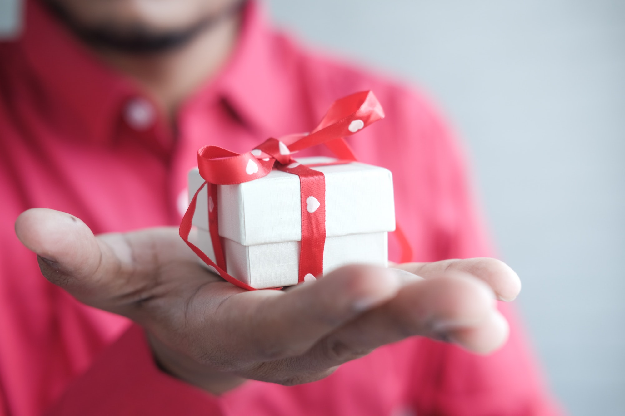 A small, white box wrapped in a red ribbon, resting in the palm of an outstretched hand.